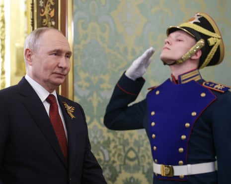 Vladimir Putin stands beside a ceremonial guard in blue uniform saluting