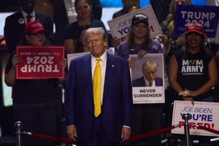 Donald Trump in yellow tie with a pained expression on his face with supporters behind him at a rally