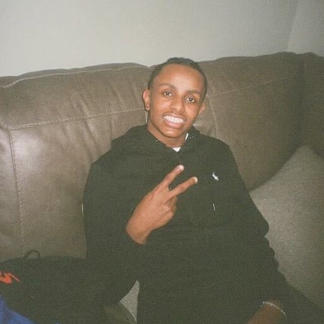 A young man sitting on a leather sofa smiles and makes a peace sign