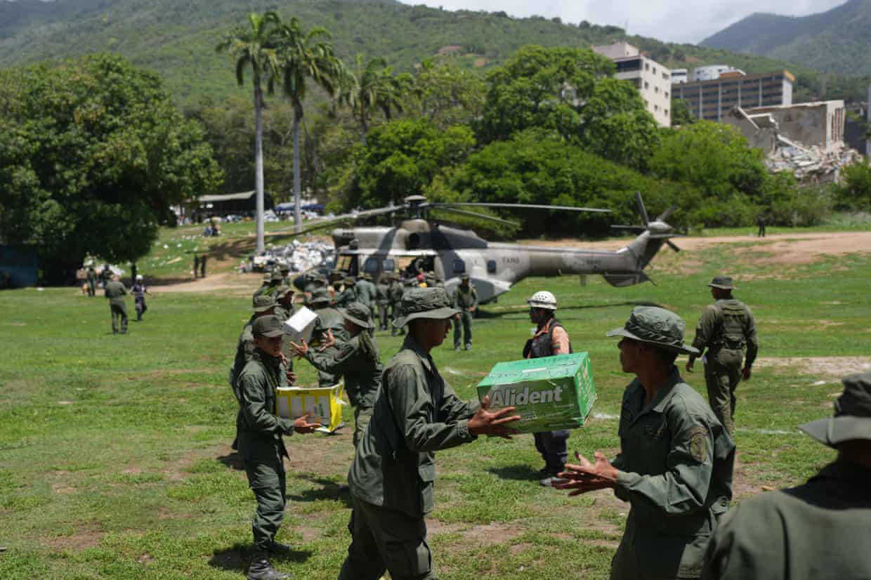 A line of soldiers passing boxes to each other, with a helicopter and trees visible in the background.