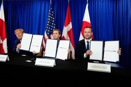 Donald Trump, Mette Frederiksen and Jens-Frederik Nielsen holding up leather bound documents at an table with the national flags of their countries behind them