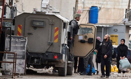 An Israeli border police member, holding a rifle, leans out of a military vehicle