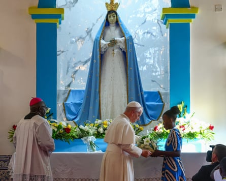 The pope being handed a bunch of flowers beneath a statue of the Virgin Mary