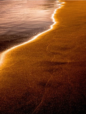 The edge of a shoreline shines orange in the light
