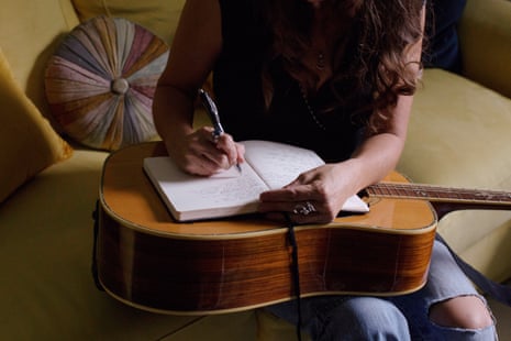 woman writing in a notebook on top of a guitar