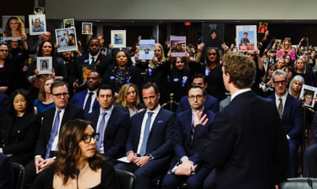 a man in his suit faces a crowd of people, many of them holding up photos of children