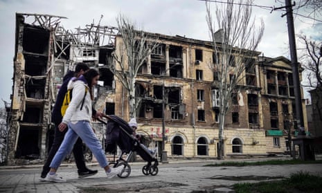 A family walk past a damaged building in Mariupol.