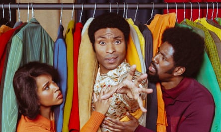 Three people stand amid a rail of clothes