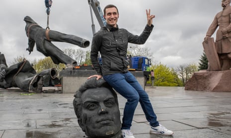 A person poses for a photo sitting on the head of the monument dismantled in Kyiv
