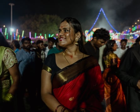 A young smiling woman standing in a festival crowd at night with neon-light decorations in the background.
