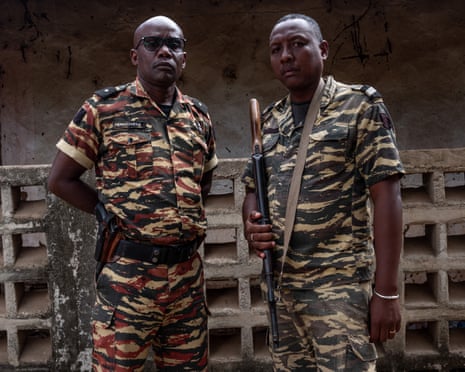 Two black soldiers in fatigues, holding guns, look at the camera