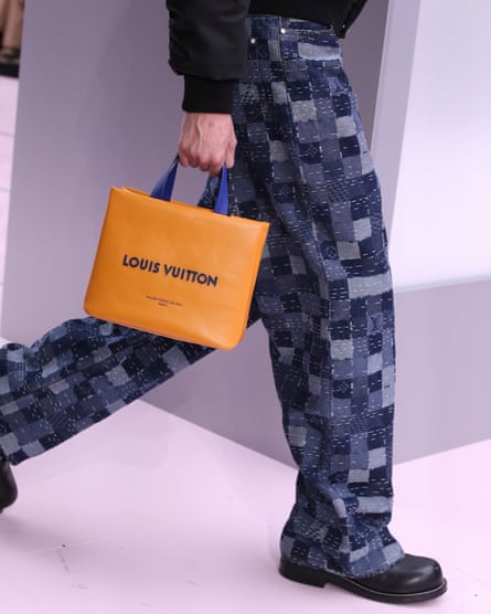 A man’s hands and legs as the man walks with an orange louis vuitton bag