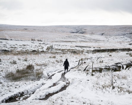 A woman walks her dog along a snow-covered path