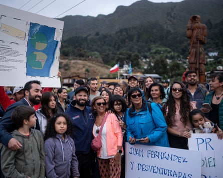 A group of people gather in front of a map of islands. Some hold handwritten banners.