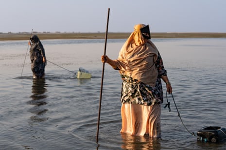 Khaleedah al-Hokmani, uma pescadora de Mahout, segura sua lança em águas rasas no porto de Shannah em outubro de 2022. Ela arrasta um recipiente plástico de combustível atrás de si para armazenar sua pesca.