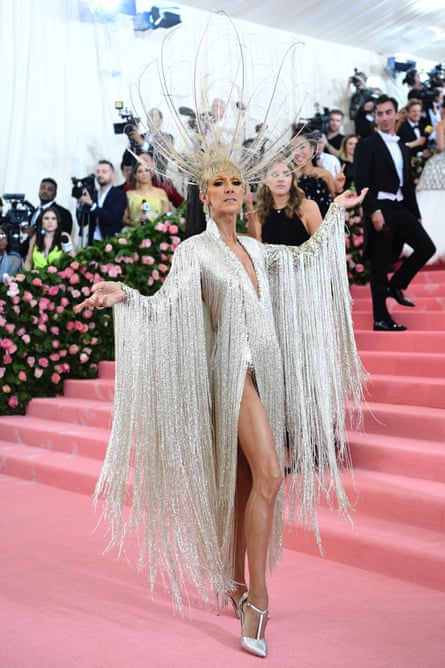 Standing at the steps of the venue, she poses while wears a shimmering silver dress, the leg cut at the waist, and a huge peacock-style headpiece