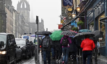 People holding umbrellas walk along a busy pavement on the Royal Mile in rainy Edinburgh