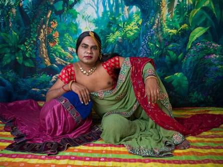 An Indian man poses in traditional anarkali-style dress with hand-painted backdrop of lush rainforest