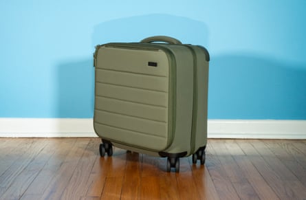 A green suitcase on a wood floor in front of blue wall
