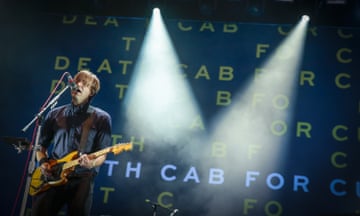 man plays guitar at microphone on stage. behind him are the words 'death cab for cutie'