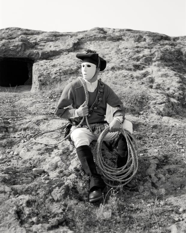 Masked man with a lariat in one hand sitting on a hill
