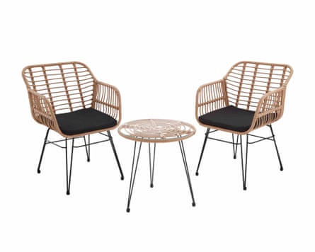 Two woven chairs with black metal legs and black seat cushions. In the middle of the chairs is a round woven table with clear glass top and three black metal legs.