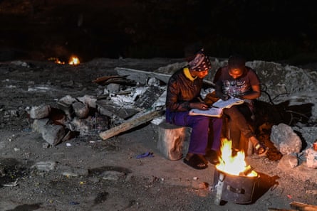 People reading outdoors by a fire