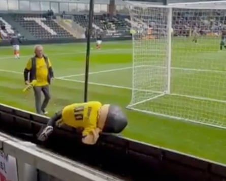 Sammy the Saint, the official mascot of St Albans City, stumbles over an advertising board before a match at Burton in November 2025.