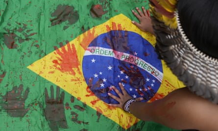 An Indigenous girl stamps her hand prints with red paint symbolising blood, on a Brazilian national flag during an Indigenous protest against violence, illegal logging, mining and ranching in September.