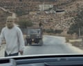 A vehicle and a masked person seen from behind a car windscreen