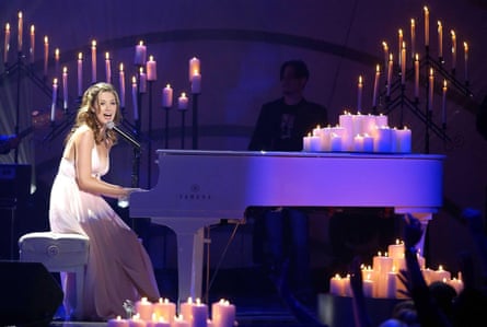 Delta Goodrem singing at a piano surrounded by candles