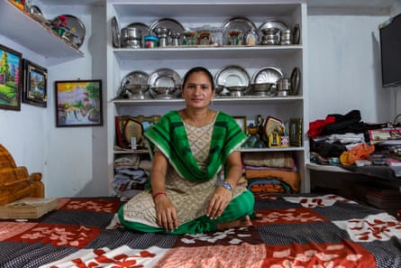 Satyavati Pandranki sits cross legged on a rug in front of a cabinet filled with silverware