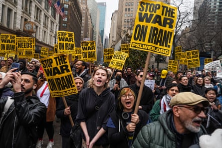 A crowd of demonstrators march, chant and hold signs that say ‘stop the war on Iran’