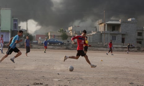 Footballers in Mosul play on as smoke rises from oil wells set on fire by Isis in October 2016.