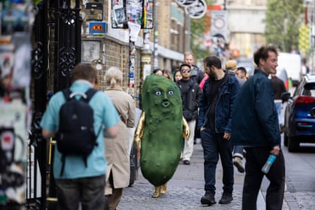 Person in green pickle suit walking along London pavement with people around