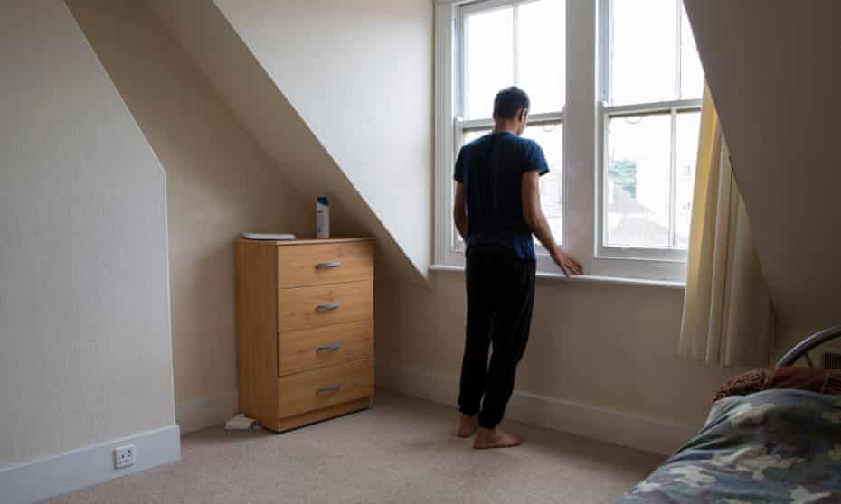 A young male, who is an unaccompanied asylum seeker, stands his bedroom in Kent, UK.