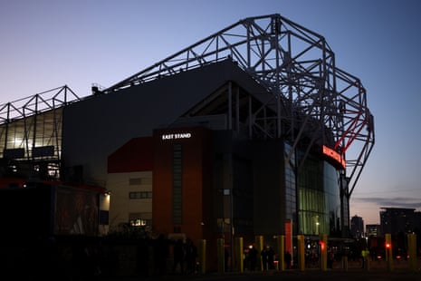 Old Trafford at dusk under a blue sky.