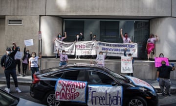 A car with signs on it in front of people in masks holding up signs stand in front of building