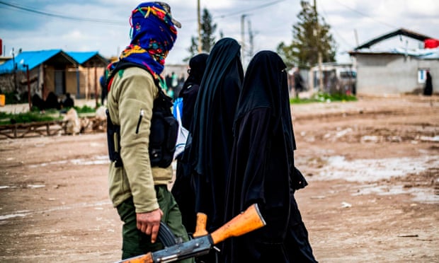 Foreign women, living in al-Hol camp which houses relatives of Islamic State (IS) group members, walk under the supervision of a fighter of the Syrian Democratic Forces (SDF) in the camp in northeastern Syria on 28 March 2019.
