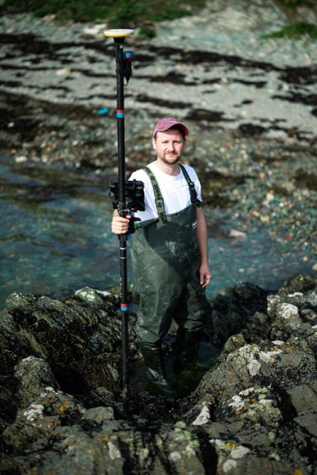Oli Thomas, project lead for Project Seagrass, stands near a rock pool holding a long, tall instrument