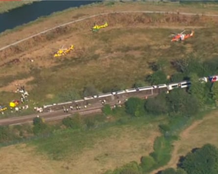 An aerial shot of three train carriages lying on their side next to the track