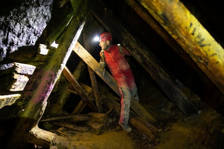 A man clambers over wooden beams installed to support the walls of the mine.