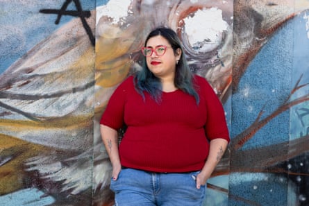 A young woman in glasses leaning against a wall with a mural