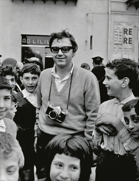 Leiter in Sicily, c1960, smiling shyly, surrounded by children, camera around his neck.
