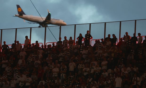 A plane flies past as fans watch the game.