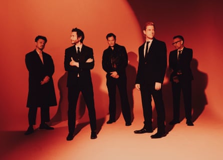 Interpol in 2026, wearing suits and posing against an orange backdrop