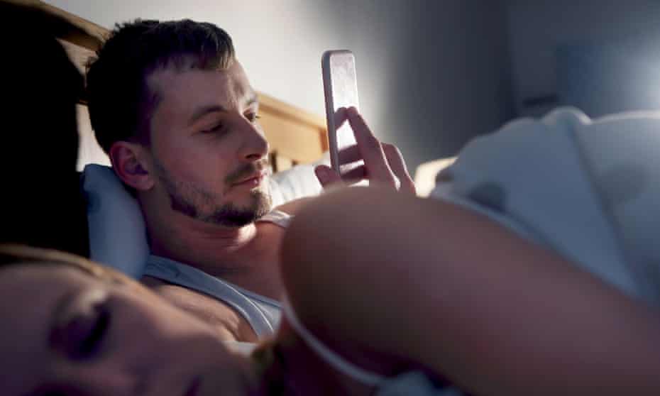 Man on his phone in bed next to sleeping partner