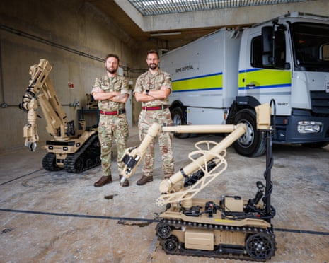 Capt Liam Kidman and Maj Andrew Boyce stand arms crossed beside a bomb-disposal robot and truck