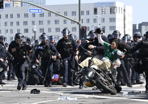 A protester appears to fall off a motorcycle with a row of police officers in the background