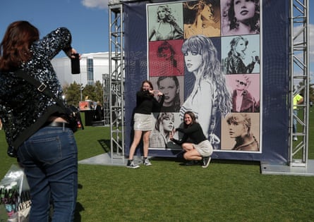 women pose in front of large poster of swift showing her during different periods of her career